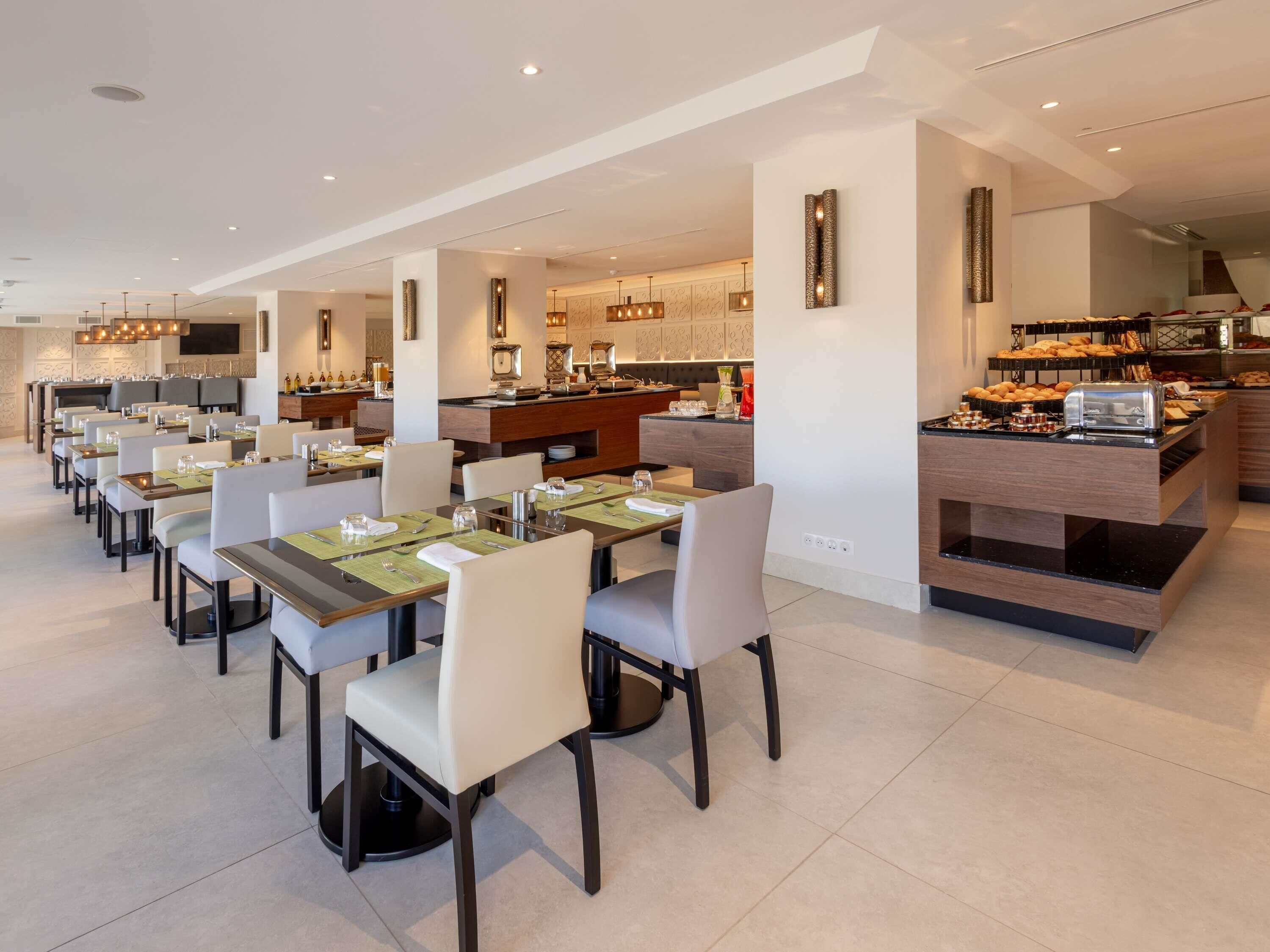 A modern dining area with multiple tables and chairs, a kitchen area with a buffet, and a bar with a coffee station.