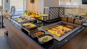 Un bufé con diversos alimentos y una zona de estar con mesas y sillas.