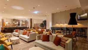 Un hall de hotel espacioso con zona de bar, arreglos de asientos y un televisor de pantalla plana grande montado en la pared.