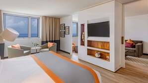 Un hotel moderno con una cama grande, un televisor de pantalla plana, una zona de estar con sillones y vistas al mar a través de amplios ventanales.