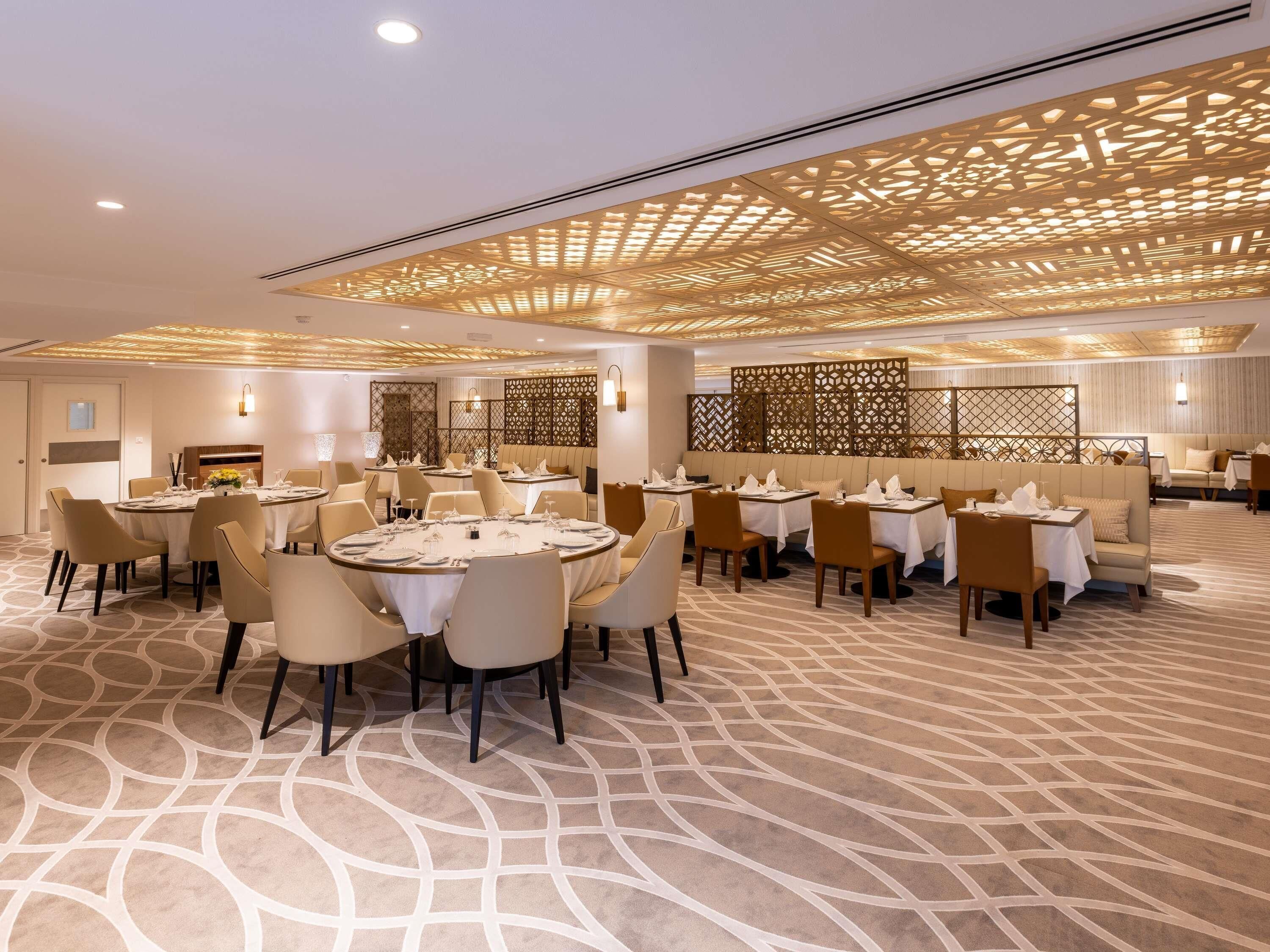 A spacious dining area with round tables, chairs, and a patterned carpet.
