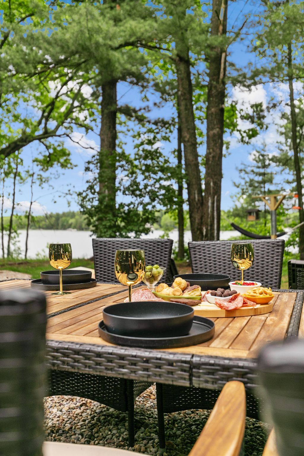 Un espace de restauration en plein air, avec des chaises en osier et une table en bois, agrémentée de verres à vin, d’olives, de charcuteries et de pain.