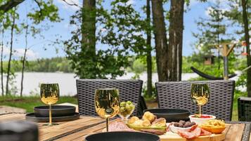 Un espace de restauration en plein air, avec des chaises en osier et une table en bois, agrémentée de verres à vin, d’olives, de charcuteries et de pain.