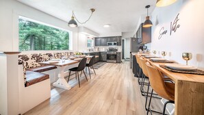 Une cuisine moderne avec un coin repas, de grandes fenêtres et une vue sur la forêt.