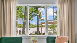 Ein Zimmer mit zwei grünen Sesseln, einem kleinen Tisch mit einer Pflanze und Blick auf einen Park mit Bäumen und einer Schaukel durch große Fenster.