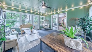 Ein gemütliches Zimmer mit einem Bett, einem Holztisch und einem Stuhl. Es gibt große Fenster und einen Deckenventilator.