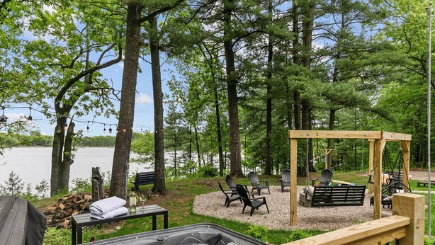 Ein Whirlpool mit einer Holzterrasse, umgeben von Sitzgelegenheiten im Freien und einem Pavillon, mit Blick auf einen See.