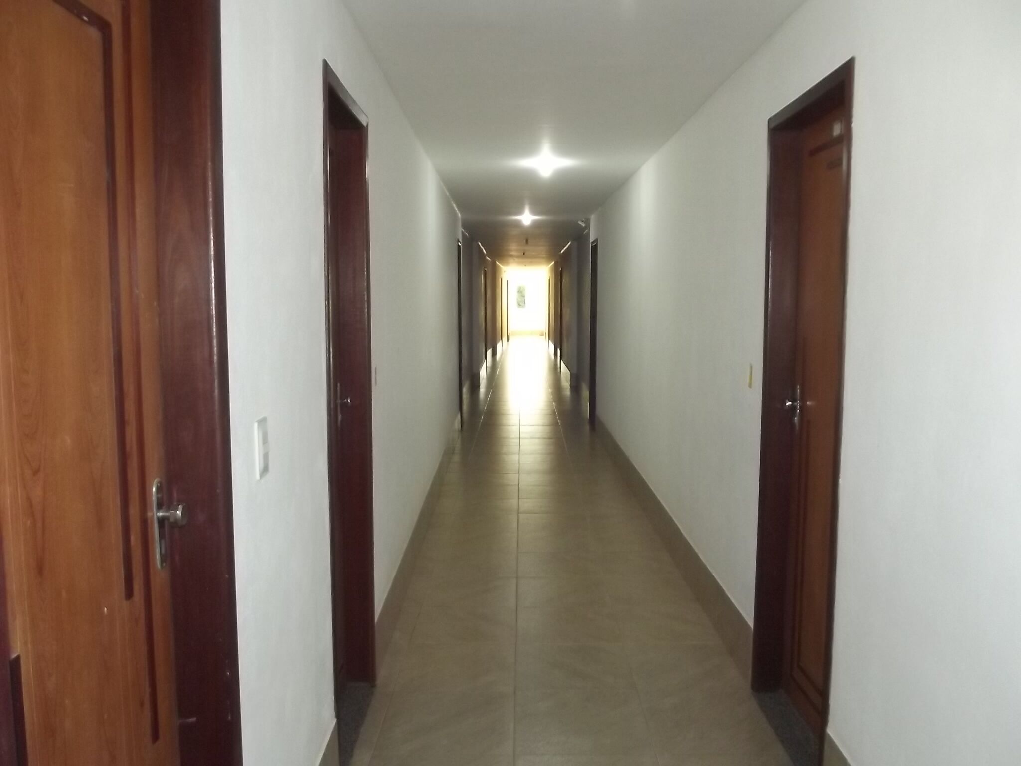 A long, narrow hallway with wooden doors on both sides and a tiled floor.