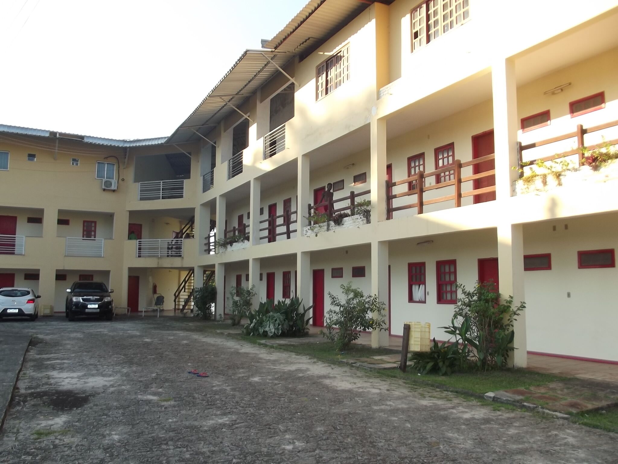 A multi-story building with balconies, a parking area, and a small garden with plants.