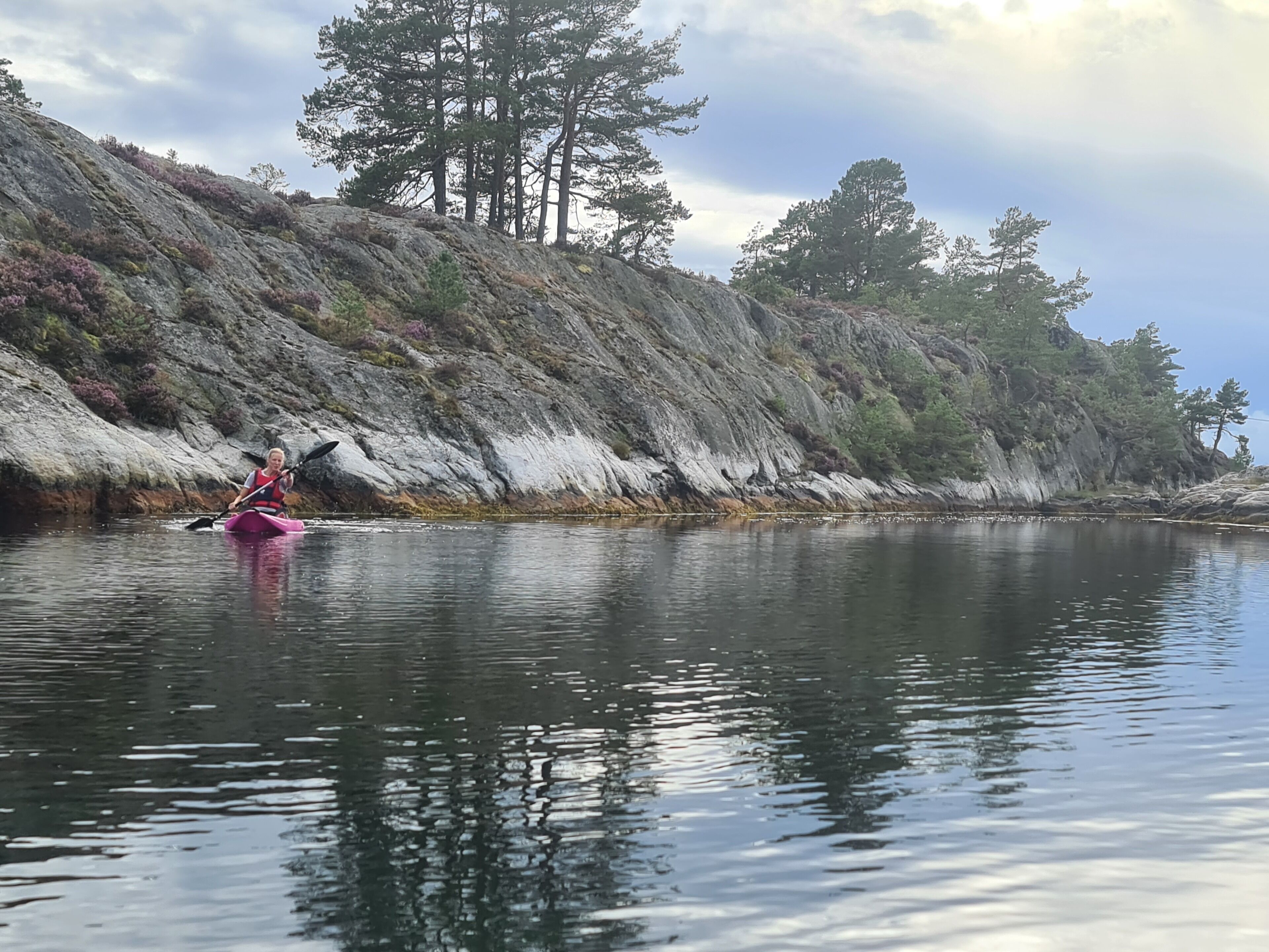 Una persona en kayak sobre aguas tranquilas, con acantilados rocosos y árboles al fondo.