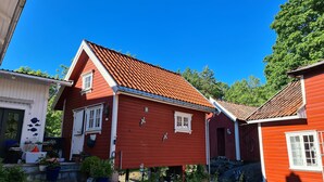 Une maison en bois rouge, avec un toit en pente, entourée de verdure et de plantes en pot.