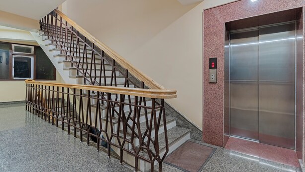 A staircase with a wooden handrail and metal balusters, leading to an elevator with a digital display. - Treebo Regal Residency A Boutique (Gangtok)