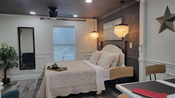 Un dormitorio con cama, escritorio, silla, ventilador de techo y ventana con persianas.
