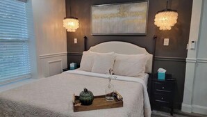 Una cama bien hecha con una bandeja de objetos, dos lámparas de pared y un cuadro sobre la cama.