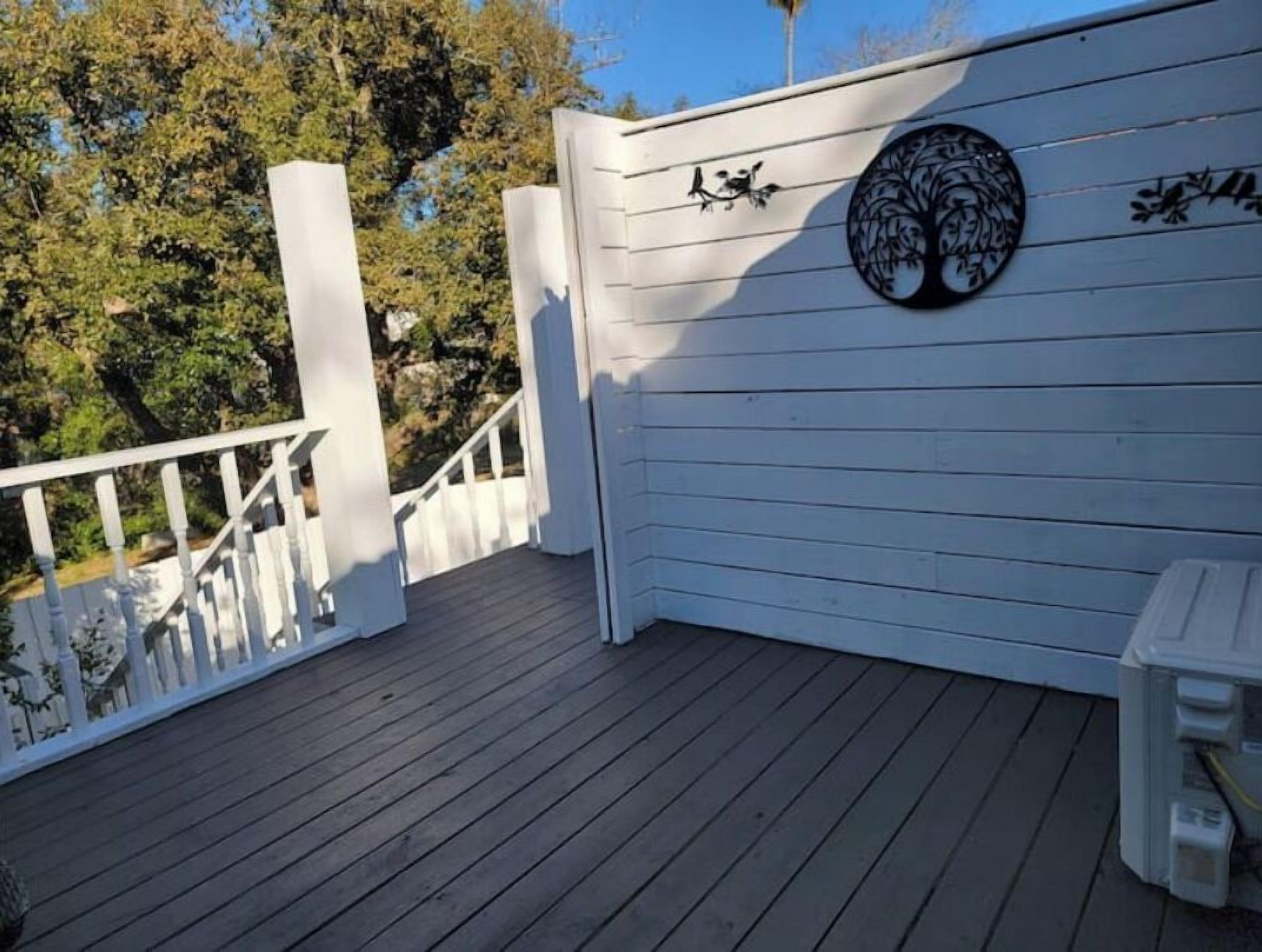 A wooden deck with white railings, a circular wall decoration, and a bench.