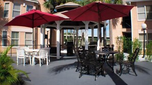 A covered outdoor patio with tables and chairs, red umbrellas, and a gazebo. - Sophisticated Retreat (Kissimmee)