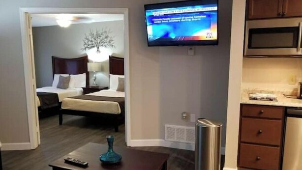 A hotel room with a bed, a TV mounted on the wall, a small table with a vase, and a trash can. - Sophisticated Retreat (Kissimmee)