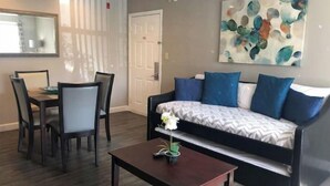 A modern living room with a sofa, a dining table with chairs, a coffee table, and a painting on the wall. - Sophisticated Retreat (Kissimmee)