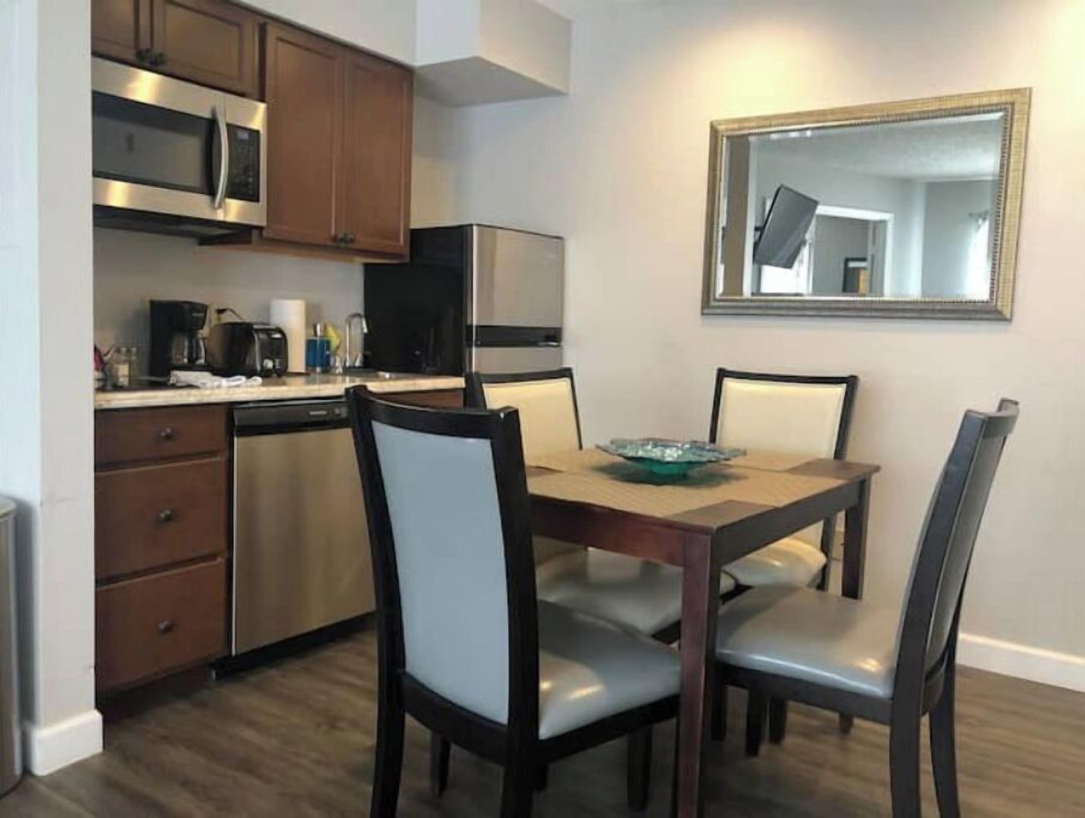 Une cuisine compacte dotée d’appareils électroménagers modernes, une table à manger avec des chaises et un grand miroir au mur.