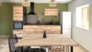 A modern kitchen with wooden cabinets, a built-in oven, and a black range hood. There is a dining table with four chairs and a vase on it.
