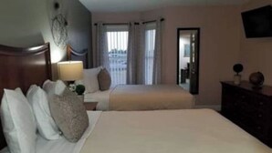 Hotellihuone, jossa on kaksi sänkyä, yöpöytä, lamppu ja lipasto.