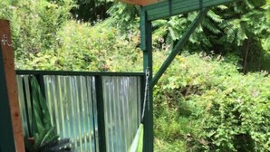 Un'amaca sospesa su un pontile di legno con ringhiera metallica e una struttura verde sullo sfondo.