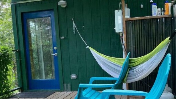 Un portico coperto con un muro verde, una porta blu e due sedie turchesi con un'amaca.