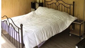 Un letto singolo con struttura in metallo, un comodino con una lampada, un quadro appeso al muro e una finestra che si affaccia sul verde.