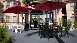 An outdoor patio with two red umbrellas, a covered seating area, and a pool. - Splash of Disney Color & Fun (Kissimmee)