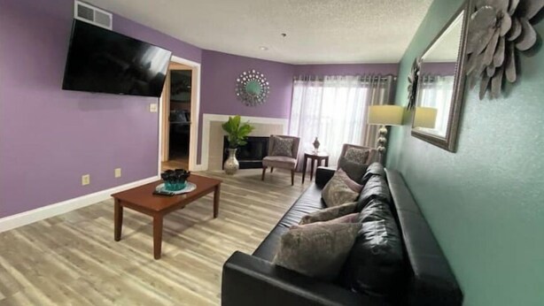 A living room with a black leather sofa, a wooden coffee table, and a television mounted on the wall. - Splash of Disney Color & Fun (Kissimmee)