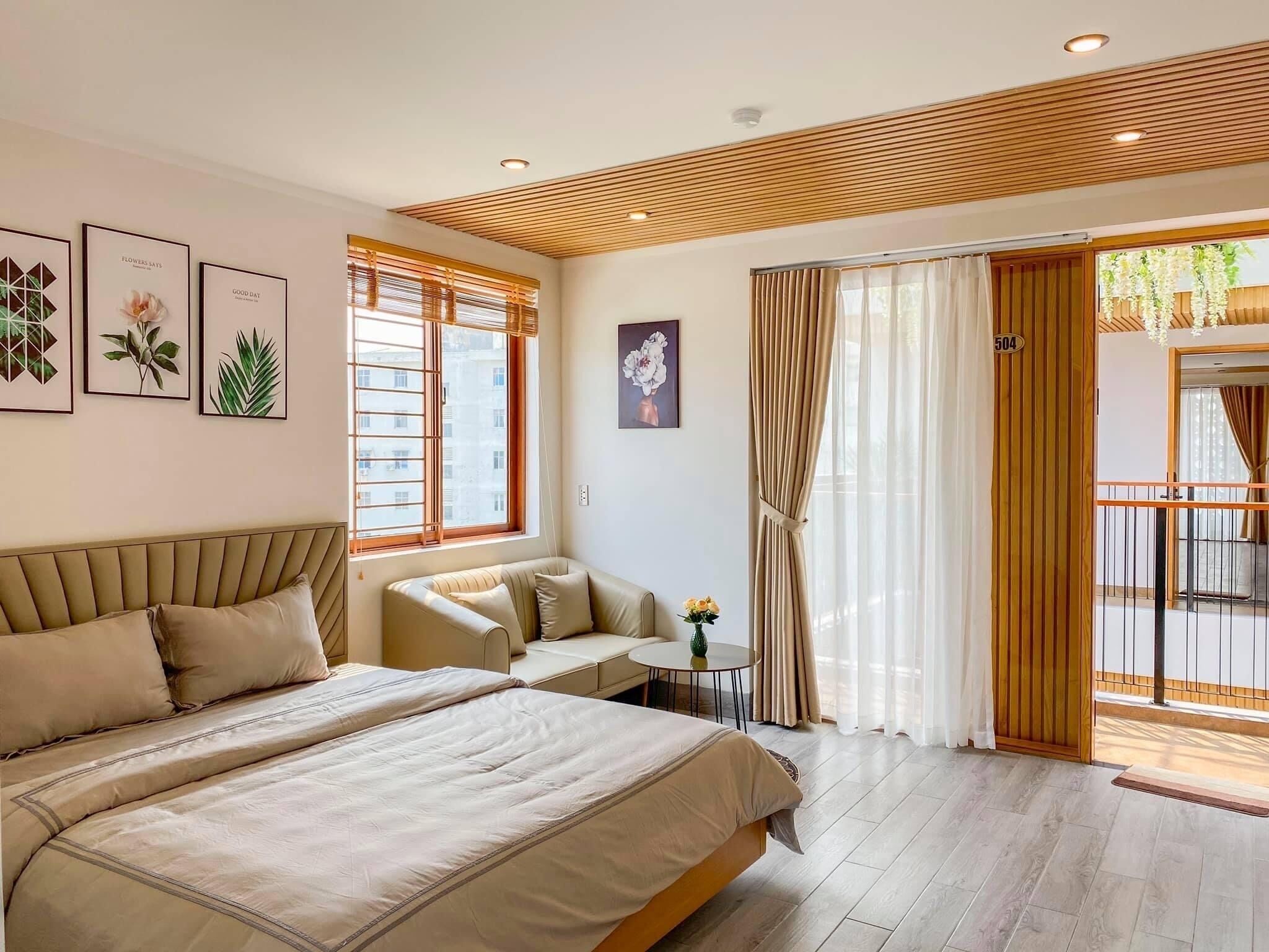 A modern bedroom with a large bed, a sofa, a small table with flowers, and a balcony with curtains.