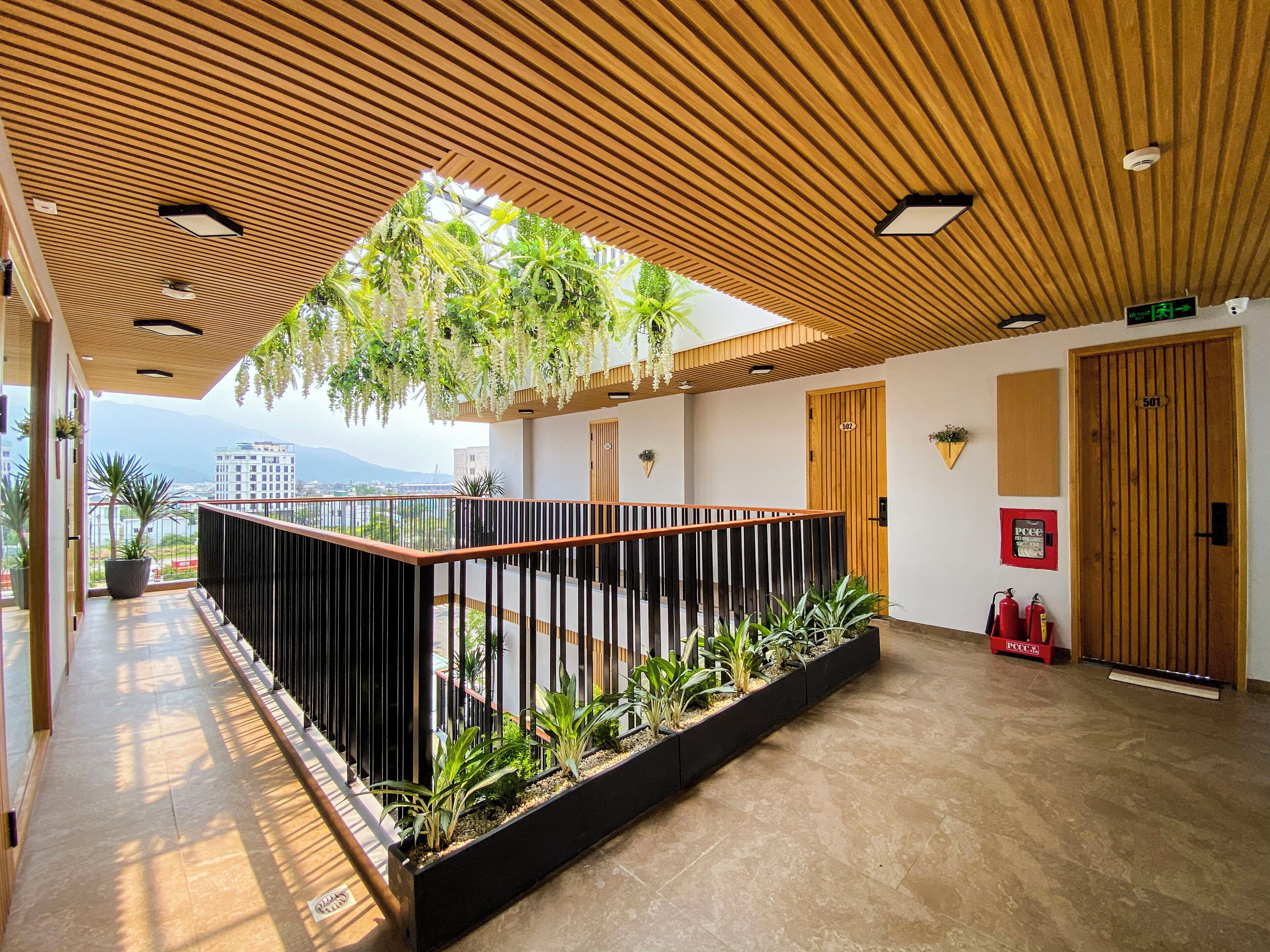 A modern interior with a wooden ceiling, a balcony with plants, a fire extinguisher, and a door marked '501'.