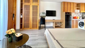 A modern bedroom with a bed, a desk, and a TV. There is a kitchen area with a washing machine and a microwave. - SALA Serviced Apartment (Đà Nẵng)