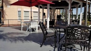 En utomhusplats med en pergola, röda parasoller och bord och stolar i metall.
