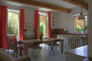 Een keuken met een houten tafel, stoelen en een uitzicht op de natuur door grote ramen.