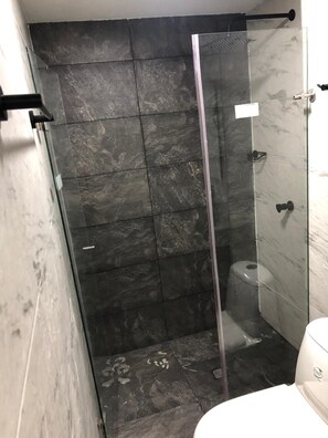 A bathroom with a glass-enclosed shower, dark marble tiles, a toilet, and a white sink.