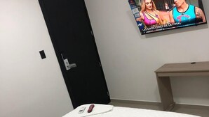 Une chambre d’hôtel avec un lit, un téléviseur fixé au mur, un bureau et une porte.