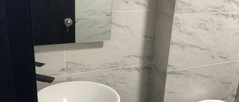Une salle de bain avec un lavabo blanc, des toilettes et un miroir.