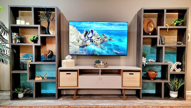 Un salon moderne doté d’un grand téléviseur à écran plat fixé au mur, de deux étagères en bois de part et d’autre, et d’un bureau central muni de deux tiroirs.