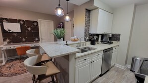 Une cuisine moderne avec des meubles blancs, un plan de travail en granit, une machine à café et un lave-vaisselle.