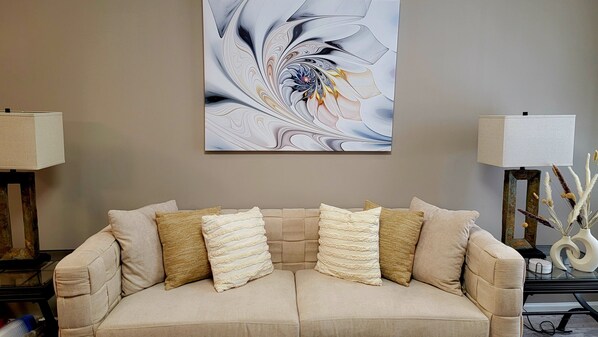 A beige sofa with multiple cushions, a large abstract painting on the wall, and two side tables with lamps and decorative items.
