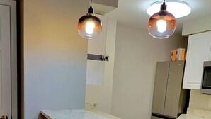 Une cuisine moderne dotée d’un îlot central, de deux tabourets de bar, d’un éclairage suspendu et offrant une vue sur la mer par une fenêtre.