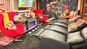 A home theater setup with a large screen, red and black leather seating, popcorn buckets, and a 'Movie Night' backdrop.