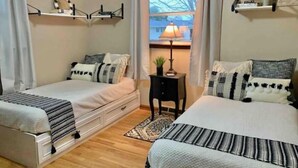 A bedroom with two beds, a small table, and a window with a view.