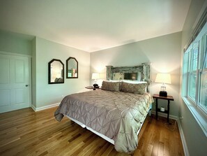 A bedroom with a large bed, two bedside lamps, a wooden nightstand, and a window with a view. - Chestnut Cottage (Highlands)