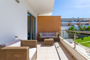 A balcony with wicker furniture, a glass balustrade, and a view of a residential area.