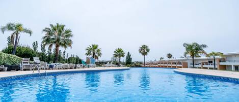 A swimming pool with lounge chairs and palm trees.