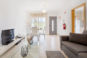 Un salon moderne doté d’un téléviseur à écran plat, d’un canapé, d’un coin repas avec une table et des chaises, et d’un espace cuisine avec un réfrigérateur.