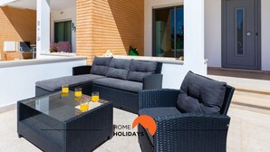 Un espace de vie extérieur moderne, doté d’une table à plateau de verre, de sièges confortables et offrant une vue sur la façade du bâtiment.
