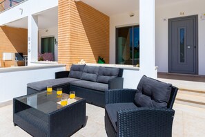 Un espace extérieur moderne, aménagé avec une table à plateau de verre, deux chaises et un canapé.
